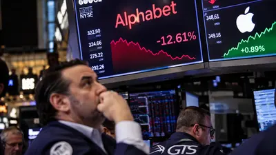 Trader on the New York Stock Exchange floor looks up at screens showing Alphabet down 12.61% and Apple up
