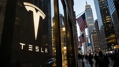 Illuminated Tesla logo on a glass facade above a busy Manhattan street with American flags and skyscrapers at dusk