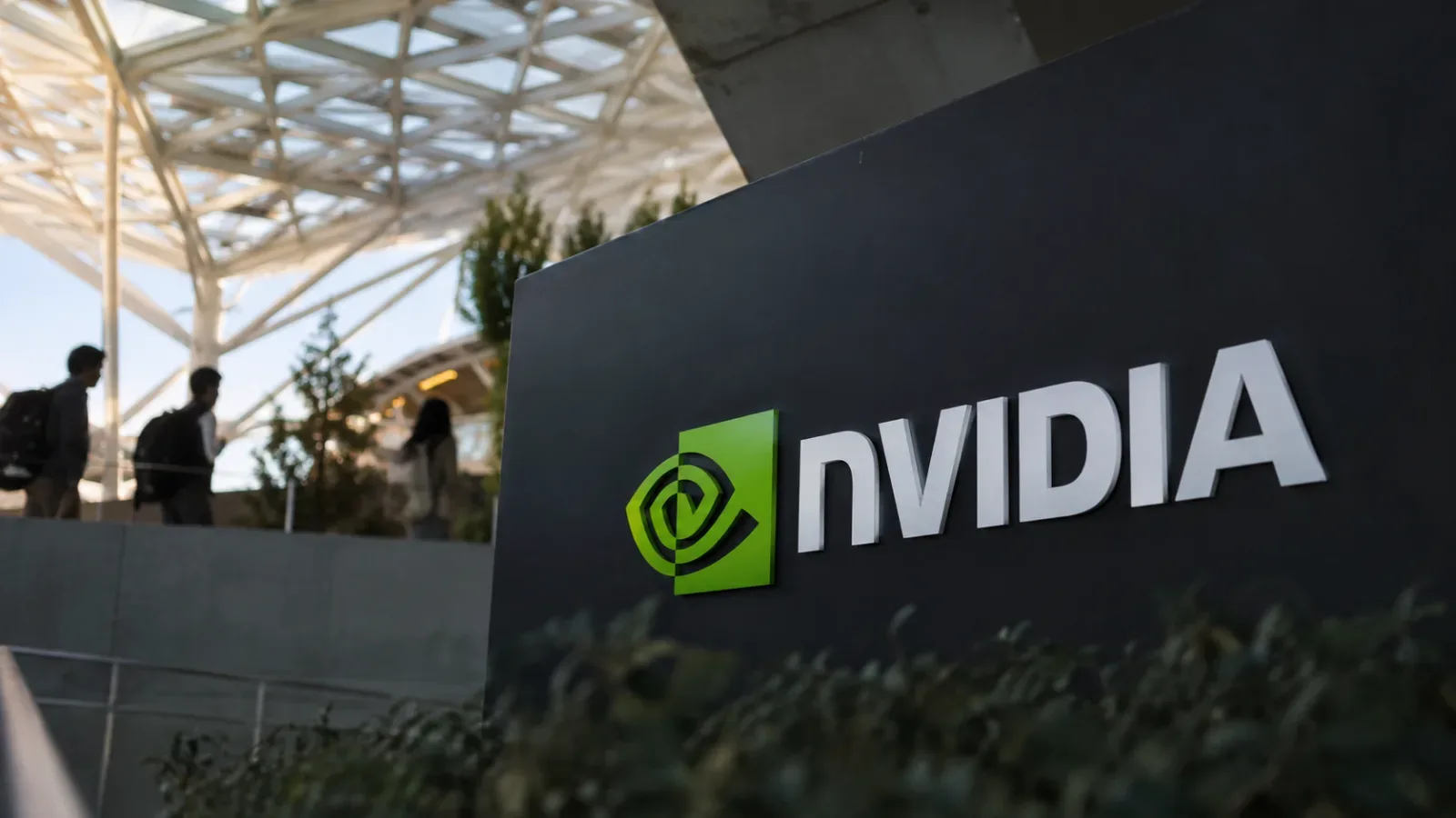 Employees walk past a large Nvidia logo sign at a corporate campus entrance